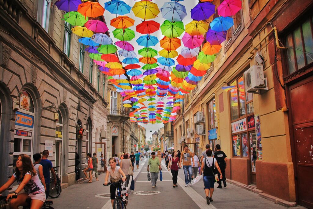 People walking down a street with colorful umbrellas in the sky 